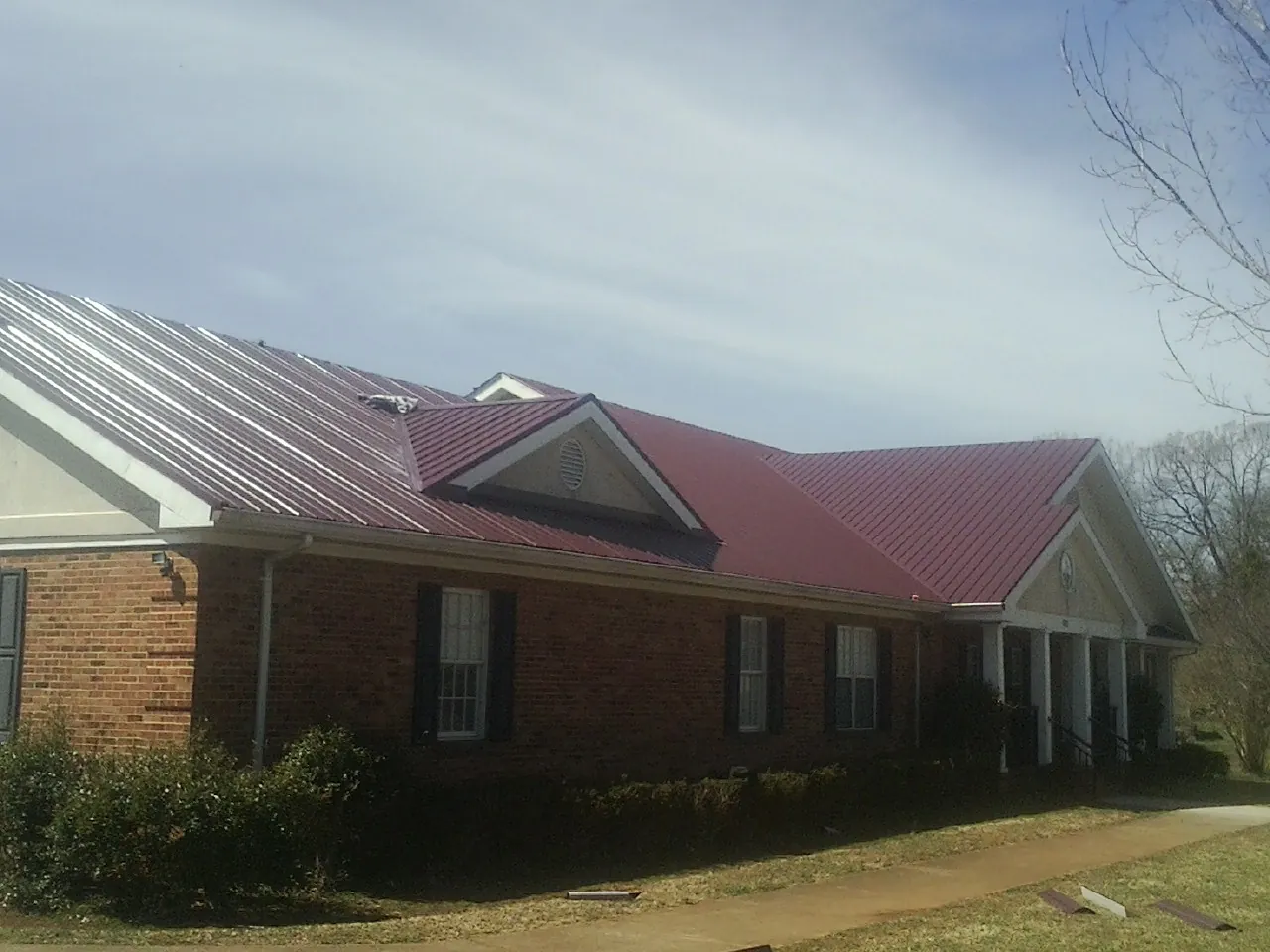 Red metal roof with gabled entries on a long brick building, from a Hail Damage Roof Repair job in Venetia