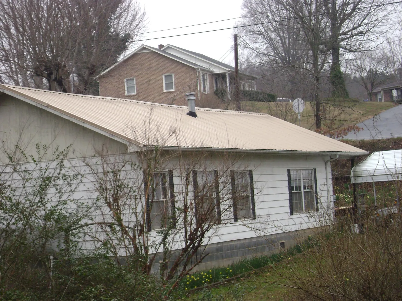 Tan metal roof on a white sided house set into a hillside — Commercial Roofing by Roofing Brothers in Venetia